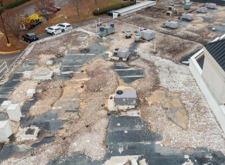 Aerial view of a deteriorating rooftop with extensive weather damage and scattered hvac units, highlighting the need for expert roof coating services.