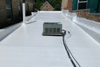 Flat roof with a newly applied white coating by Expert Roof Coating Services and a central air conditioning unit.