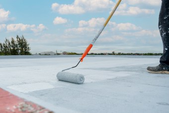Applying expert roof coating services on a flat roof with a paint roller.