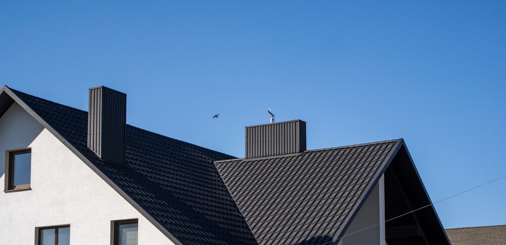 How long does a metal roof last - A modern house with a dark gray tiled roof, several chimneys, and a clear blue sky in the background.