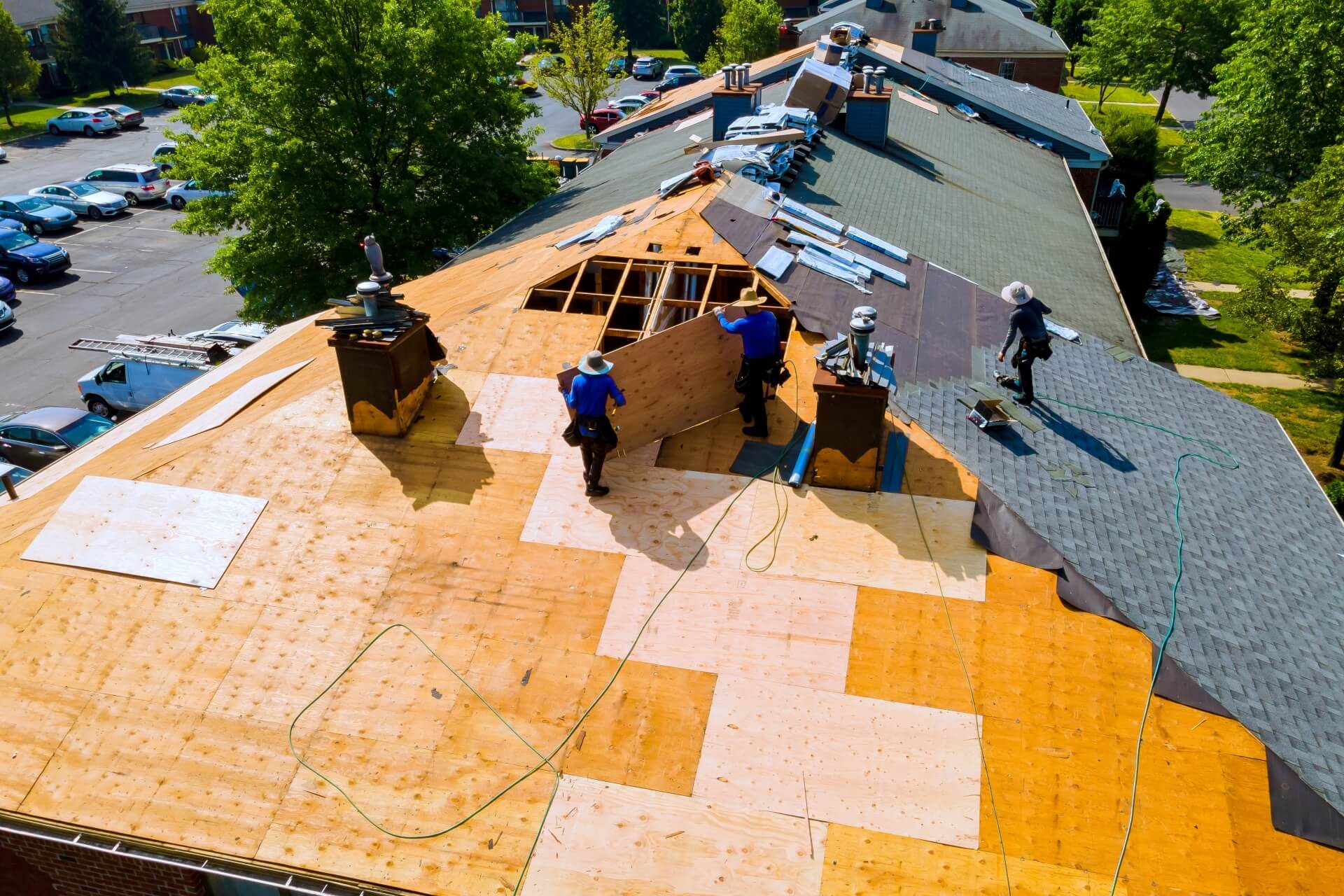 Rooftop view of workers installing plywood and shingles on a commercial roof.