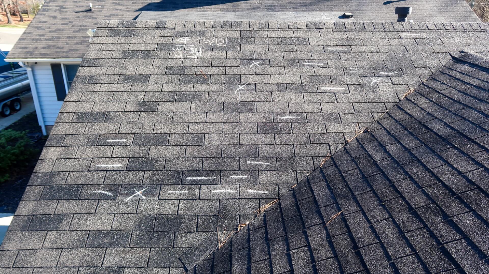 Dark grey shingle roof with chalk 'X's for inspection and replacement guide.