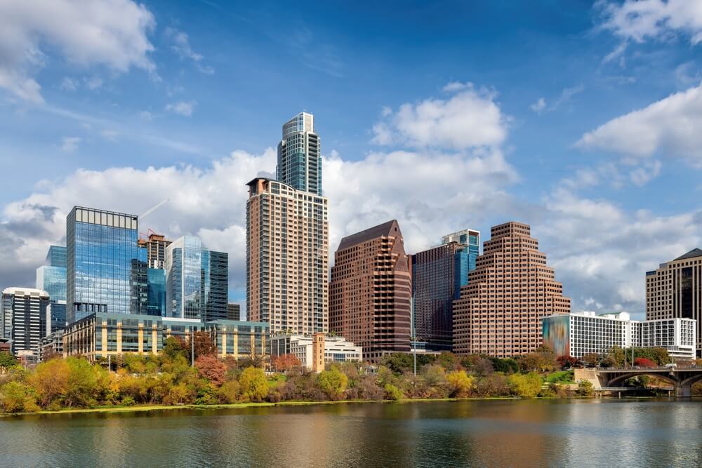 City skyline with modern and historic buildings, diverse roofs, water, greenery, partly cloudy sky.