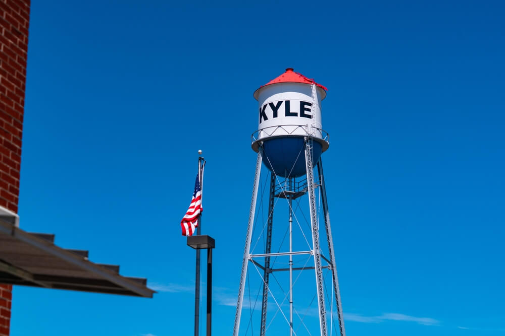 Water tower labeled "KYLE" reflecting on nearby commercial roofing.