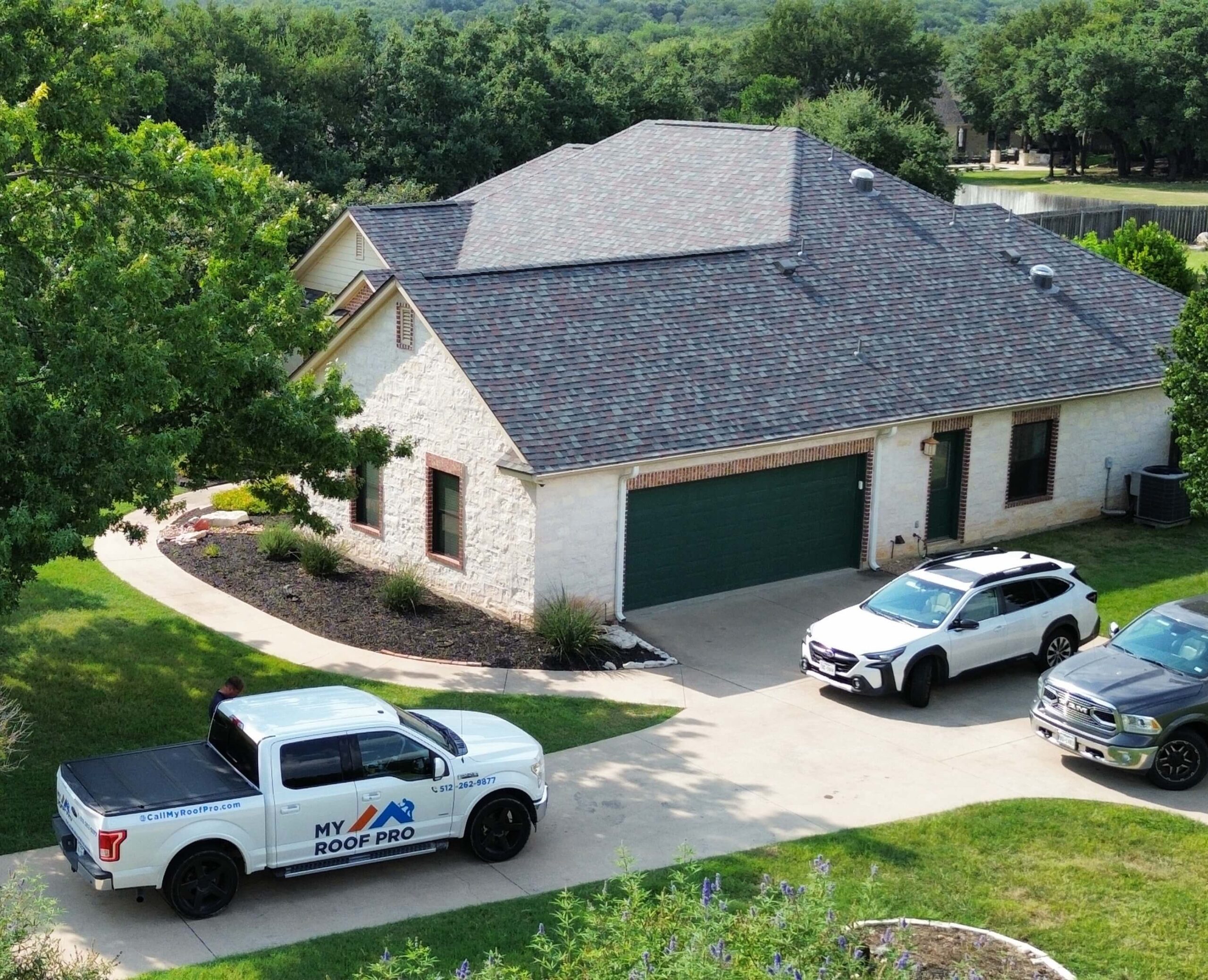 Commercial gray-roofed house with green garage in wooded area, featuring "My Roof Pro" truck.