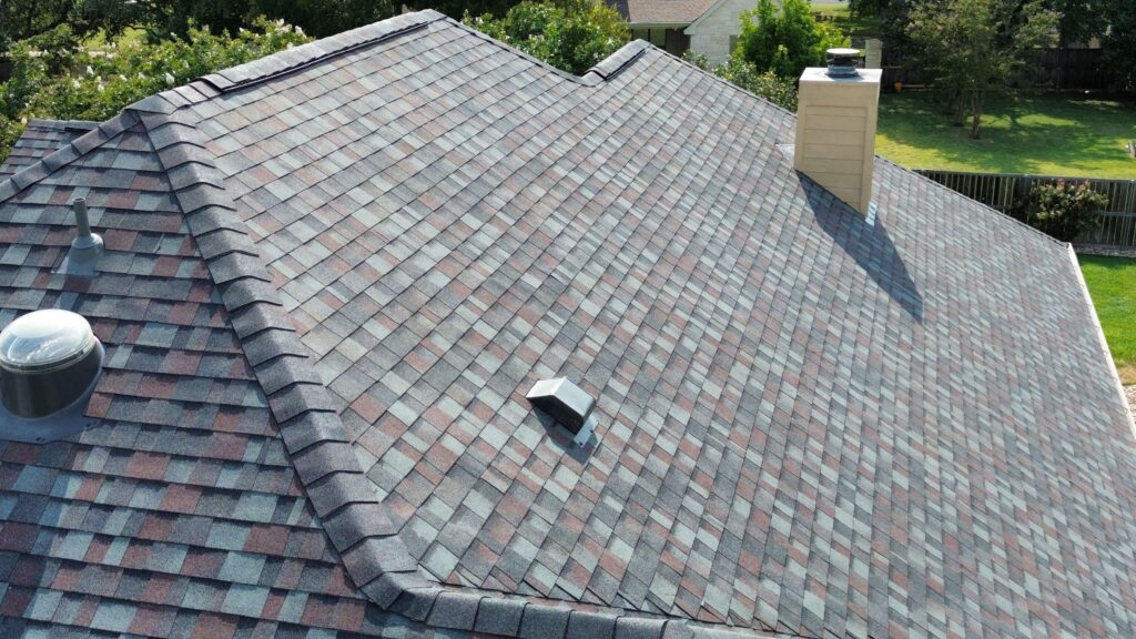 Residential shingle roof with chimney and vents amidst landscaping