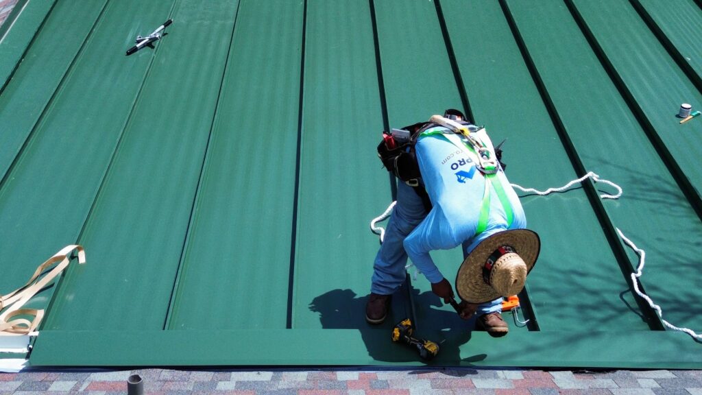 Worker in blue: Installs green metal panels on commercial roof