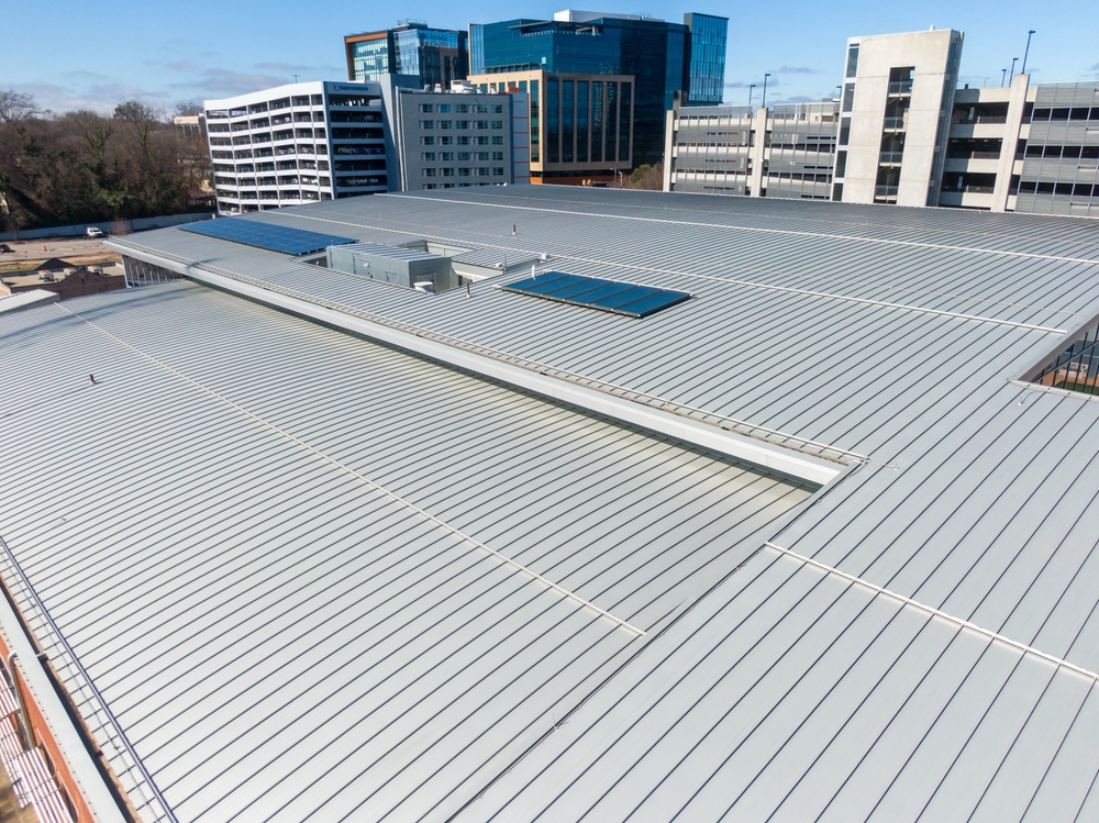 The Benefits of Metal Roofing for Homes in San Antonio. Industrial rooftop with metal sheets and solar panels; office buildings and trees nearby.